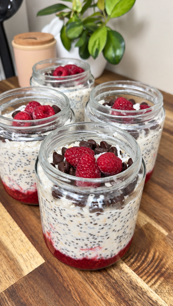 Jam lamington overnight oats in glass jars with raspberries and dark choc chips