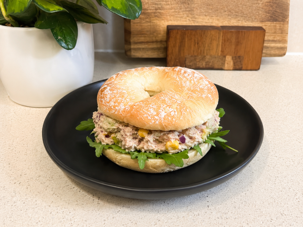 Tuna avo smash bagel on a black plate with rocket and sweetcorn